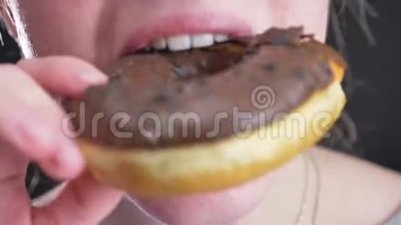 女孩的特写肖像微笑地咬着咀嚼着美味的釉色棕色甜甜圈黑色的巧克力片视频的预览图