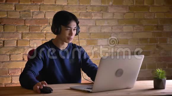 戴着笔记本电脑的年轻韩国男学生戴着耳机兴奋地举起手臂的特写照片视频的预览图