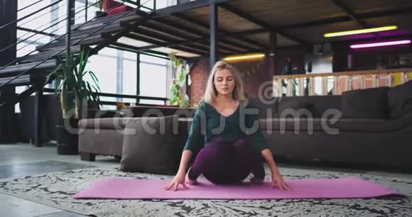 美丽的金发女人早上在家里练习瑜伽她伸展身体有一个健康的生活方式视频的预览图