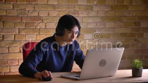 年轻迷人的韩国男学生戴耳机的特写镜头在笔记本电脑上检查心烦意乱心烦意乱视频的预览图