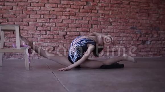 灵活的十几岁女孩在砖墙前的工作室里热身双腿分开前腿靠在木头上视频的预览图