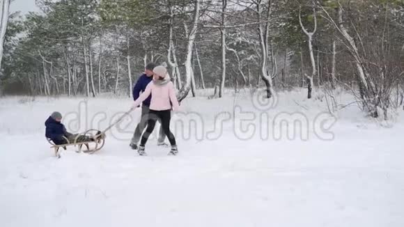 幸福的家庭在下雪的冬天滑雪父亲和母亲在下雪时和儿子拉雪橇绳索户外男孩雪橇视频的预览图