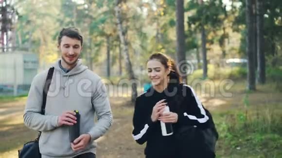 年轻有魅力的女孩和她的朋友聊天在户外训练后笑着拿着运动袋在公园里散步视频的预览图
