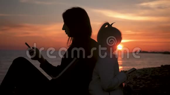 剪影母女在日落时在海滩上使用手机技术理念生活方式视频的预览图