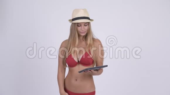 穿着比基尼的年轻女游客使用数码平板电脑看上去很惊讶视频的预览图