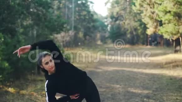 穿着现代运动服装的漂亮黑发女子独自在公园里锻炼活动着手臂和身体享受着新鲜的感觉视频的预览图