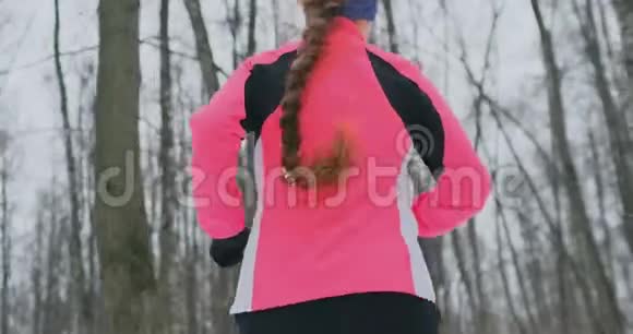 冬天一个年轻的女人穿着一件粉红色的夹克穿过公园从后面看视频的预览图