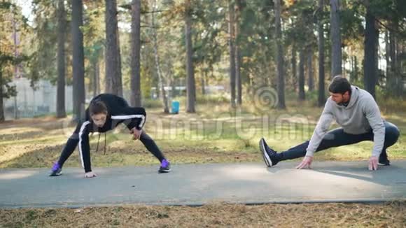 年轻的帅哥和女朋友一起在公园训练在温暖的秋日伸展双腿穿着时髦视频的预览图