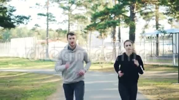 在秋天的一天男生和女生穿着现代运动服一起在公园里跑步常青松视频的预览图