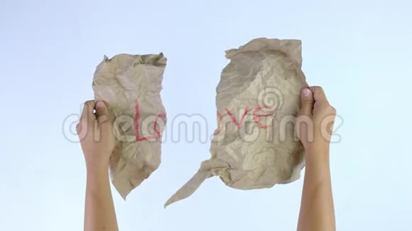 特写镜头的双手移动了一张半张皱巴巴的牛皮纸上面写着爱字孤立在白色的背景上埃米尔视频的预览图