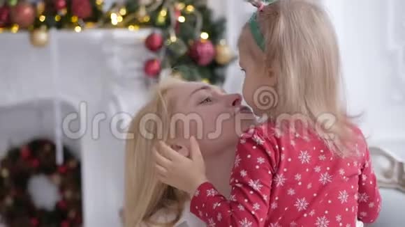 在一个装饰着圣诞装饰品的房间里一个女人把她的小女儿抱在怀里吻她视频的预览图