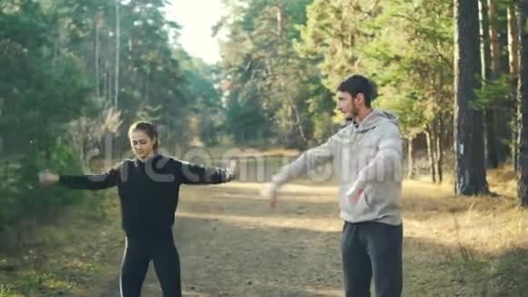 可爱的女孩正在公园里做运动她的男朋友在温暖的阳光下一起训练时热身手腕和手臂视频的预览图