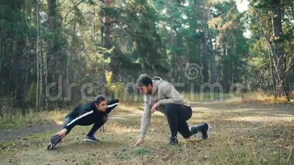 年轻的丈夫和妻子一起在公园训练在温暖的秋日穿着时髦的运动服装伸展双腿视频的预览图