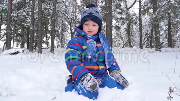 一个快乐的小男孩坐在冬天的公园或森林里的雪地上笑自然的娱乐和游戏儿童视频的预览图