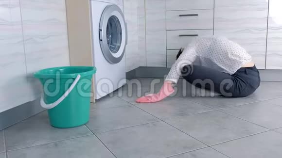 穿着粉红色橡胶手套的女人用布洗厨房家具坐在地板上侧视视频的预览图