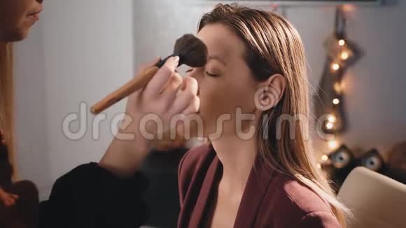 化妆师用一个大刷子粉涂在一个白人金发模特的脸上化妆生意的女人关于视频的预览图