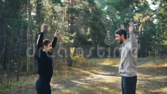 这对年轻夫妇正在公园里做户外运动手臂旋转微笑着享受热身和良好的陪伴视频的预览图
