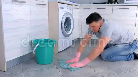穿着橡胶手套的不高兴的疲惫的男人在厨房里洗和用力地摩擦地板侧视视频的预览图