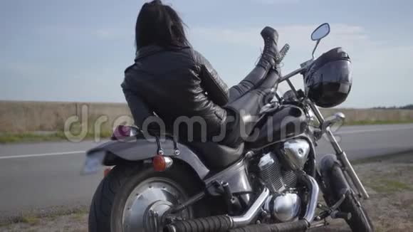 可爱的白种人女人穿着黑色皮夹克和裤子躺在一辆经典的摩托车上爱好旅游和活动视频的预览图