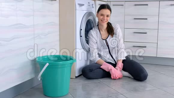 幸福的女人在厨房地板上戴着粉红色的橡胶手套清洁后看着相机视频的预览图
