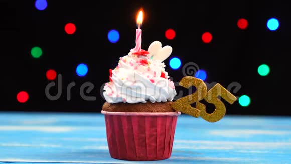 美味的生日纸杯蛋糕在五颜六色的模糊灯光背景下有着燃烧的蜡烛和25号蜡烛视频的预览图