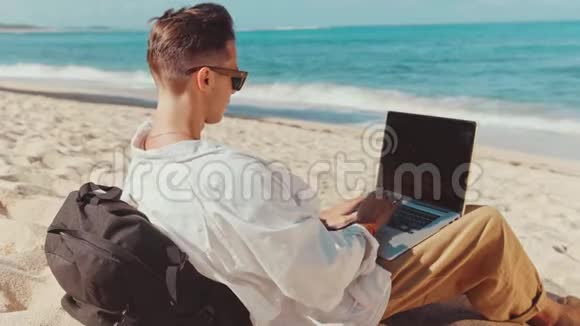 近距离拍摄年轻的职业自由职业者或游客赤脚躺在沙滩上远距离工作视频的预览图