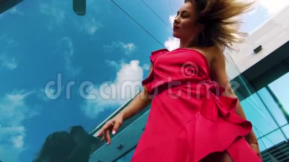 低角度的金发女郎红色舞蹈与玻璃表面反射天空视频的预览图