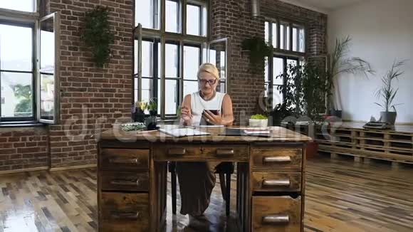 漂亮的商务女性坐在桌子旁在现代办公室工作时在平板电脑上打字视频的预览图