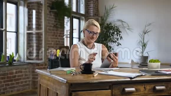 古典风格办公室里一位中年金发女郎坐在一张漂亮的木桌旁的肖像女人笑着看着视频的预览图