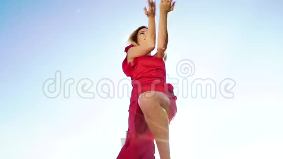 低角度拍摄迷人的金发女郎穿着红色裙子在蓝天上跳舞视频的预览图