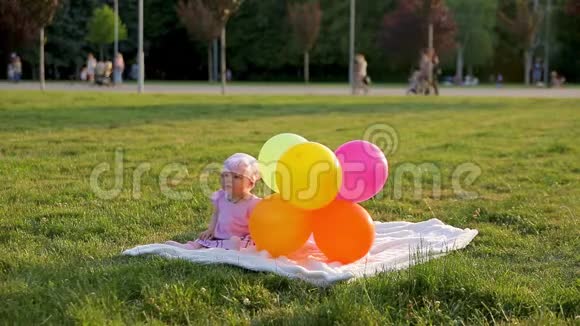 可爱的小女孩坐在城市公园的草地上旁边放着气球然后气球飞走了妈妈把它们带回来视频的预览图