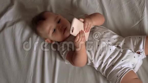 小可爱的宝宝躺在床上两腿抽搐玩智能手机视频的预览图