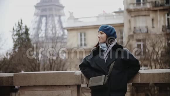 穿着贝雷帽和外套的时髦女人站在巴黎埃菲尔铁塔旁的大街上视频的预览图