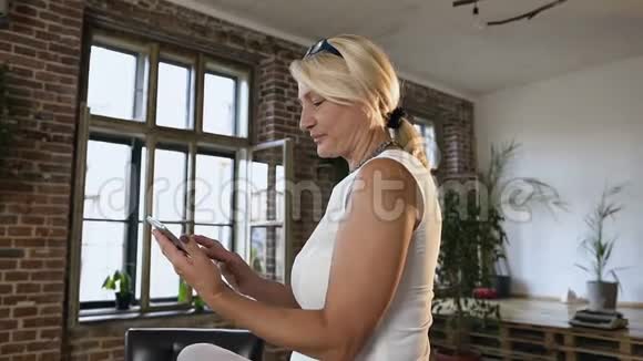 漂亮的中年妇女在办公室坐在桌子上时使用平板电脑金发女人翻页视频的预览图