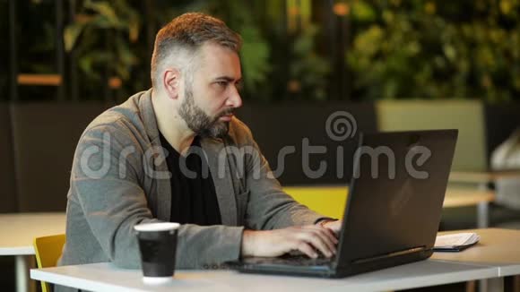 年轻留胡子的嬉皮士企业家在咖啡桌上的沙发使用笔记本电脑与空白屏幕表式笔记本视频的预览图