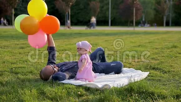 爸爸拿着五颜六色的气球躺在白色的毯子上他可爱的小女儿摘下爸爸的眼镜在公园里打他视频的预览图