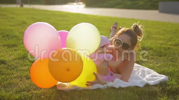 年轻的母女躺在公园草地上的白毯子上在灿烂的阳光下玩气球视频的预览图
