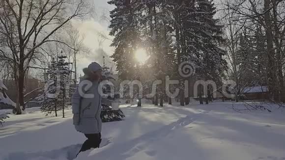 在弗罗斯特冬季公园一个戴着灰色帽子和灰色羽绒服的女人从一个透明的桶里倒开水视频的预览图