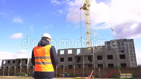 一名身穿黑色制服的男工程师戴着头盔和信号背心在一个建筑工地的平板上写下并标记视频的预览图