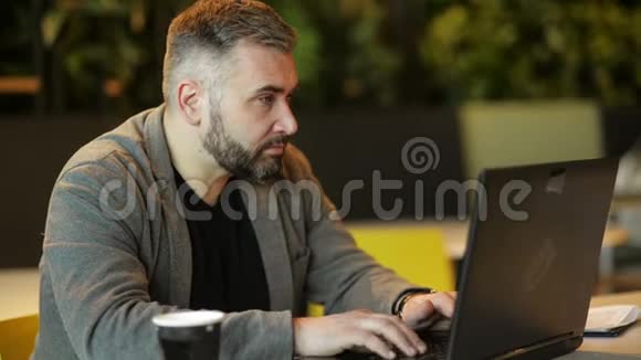 年轻留胡子的嬉皮士企业家在咖啡桌上的沙发使用笔记本电脑与空白屏幕表式笔记本视频的预览图