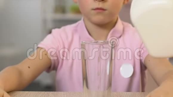 用手往玻璃杯里倒牛奶男孩愉快地喝健康的膳食维生素视频的预览图