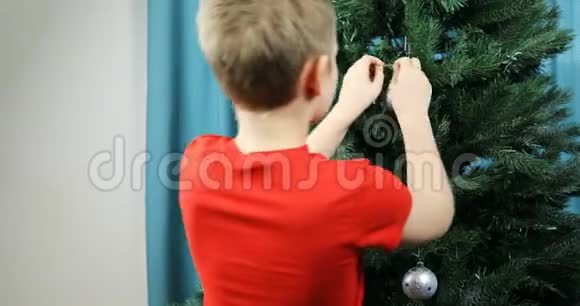 一个男孩用一个大的节日舞会装扮一棵绿色的圣诞树视频的预览图