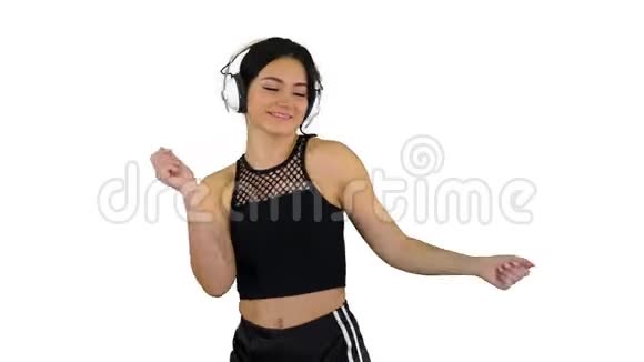 年轻快乐的运动女人听着耳机里的音乐在白色的背景下跳舞视频的预览图