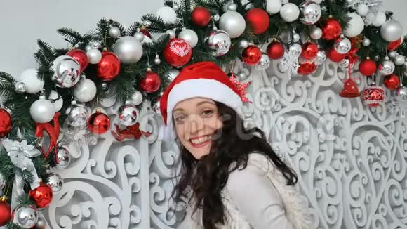 圣诞老人戴着红色圣诞帽的快乐女孩在圣诞装饰的摄影棚里亲吻镜头视频的预览图