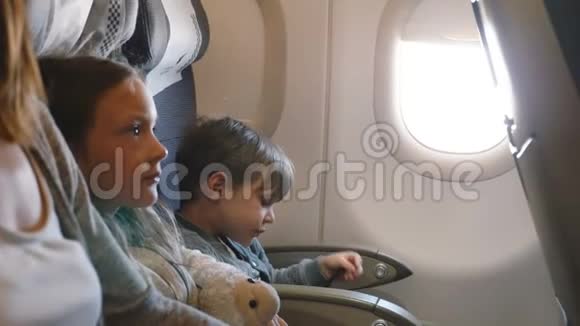 从侧面看小无聊的男孩和女孩在飞机飞行中娱乐自己去度假与家人视频的预览图