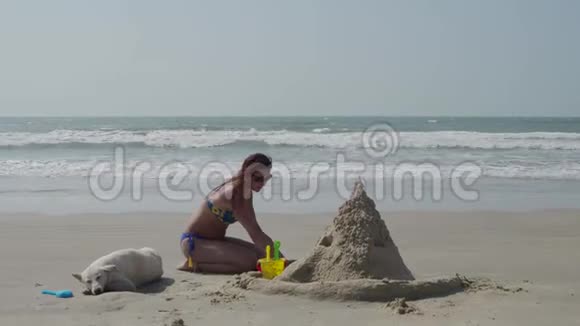 一个穿泳衣的年轻女孩在海滩上建造了一座沙堡4K视频的预览图