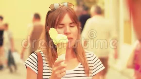 年轻美丽的女人吃冰淇淋沿着拥挤的旅游街散步夏天温暖的颜色视频的预览图