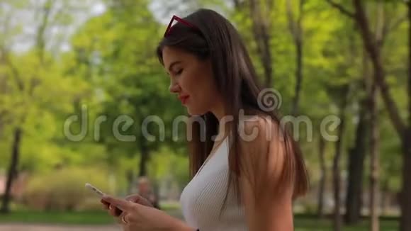夏季公园智能手机上的女性阅读信息视频的预览图