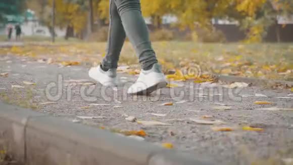 一个年轻女孩穿着运动鞋在公园的落叶上的脚秋天的概念视频的预览图