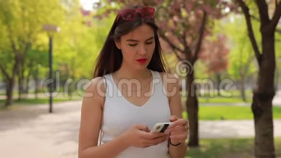 夏季公园智能手机上的女性阅读信息视频的预览图
